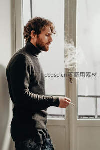 卷发男子窗边沉思抽烟