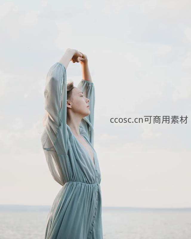 海风中伸展双臂的蓝裙女子