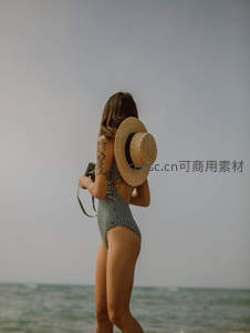 泳装女子戴草帽持相机漫步沙滩