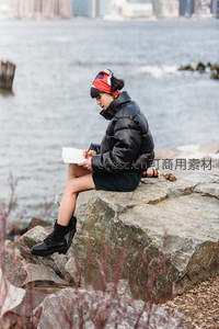 水边岩石上专注书写的城市女子