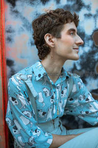 卷发青年倚墙微笑，猫咪印花衬衫吸睛