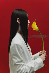 红墙前白衣女子轻嗅黄花