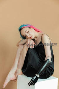 彩发女子蜷坐方块上，机械臂相伴展现独特美感