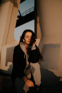 夕阳下卷发女子倚墙沉思