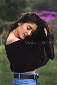 户外花丛中黑衣女子轻抚秀发，柔美自然姿态