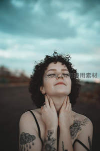 卷发纹身女闭眼仰望天空，云下释放自我的艺术时刻