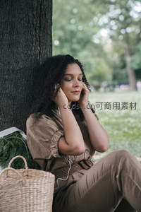 卷发女子树下戴耳机享受音乐