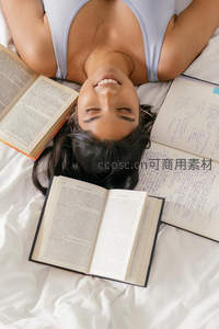 女孩躺卧床榻，书籍环绕笑容灿烂