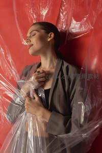 红幕前女子裹塑料膜，沉静闭目姿态