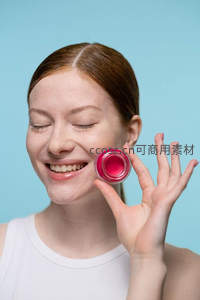 微笑女子手持粉色唇膏，背景为浅蓝色