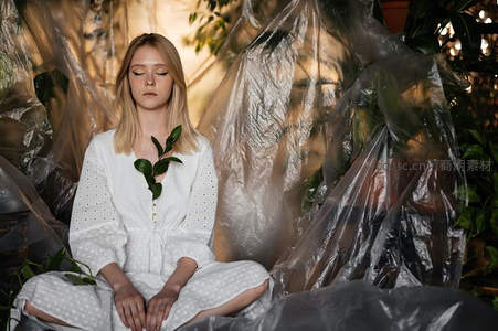 女子静坐植物环绕的透明塑料布中