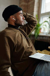 男子戴耳机闭目养神，膝上放着笔记本电脑