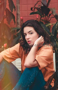 橙衣少女坐椅凝思，绿植环绕显惬意