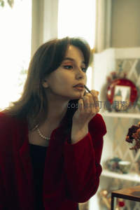 红衣女子窗边描画唇妆的静谧时刻