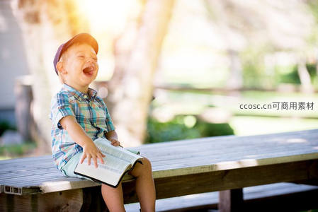小男孩坐长凳上捧书大笑