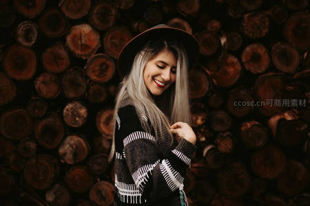 银发女子戴帽倚靠木堆微笑