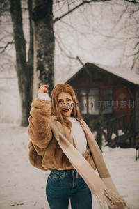雪地木屋前红发女子欢笑跳跃