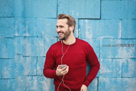 蓝墙前微笑听歌的男子