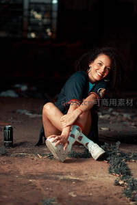 卷发女孩废墟中微笑，身旁放着能量饮料罐