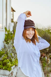 戴帽女子在庭院伸展，阳光洒满白衬衫