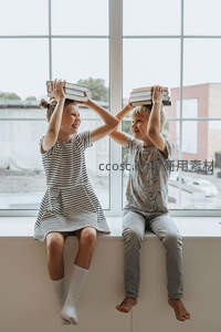 孩童窗边嬉戏，头顶书本欢笑