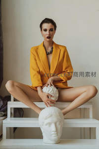 黄西装女子盘坐阶梯手抚雕塑头像