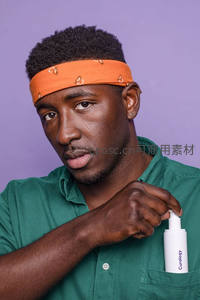 男子手持护肤喷雾，橙色头巾搭配绿衬衫