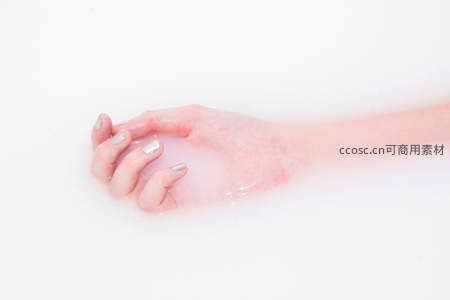 浸泡在乳白色液体中的手部特写，指甲闪耀银色光泽