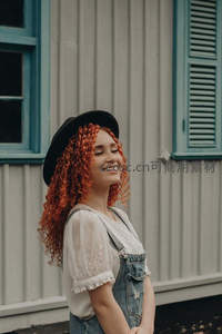 红卷发女孩戴帽微笑于复古建筑前