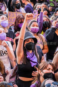 女性抗议者高举拳头，紫色口罩下的坚定力量