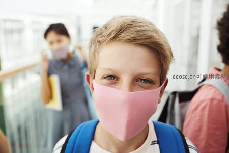 金发男孩戴粉口罩，校园走廊里微笑凝视镜头