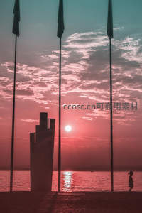 日落时分海边旗杆旁孩童漫步剪影