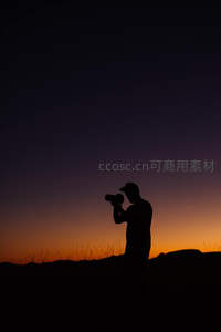 摄影师剪影于黄昏山巅专注拍摄