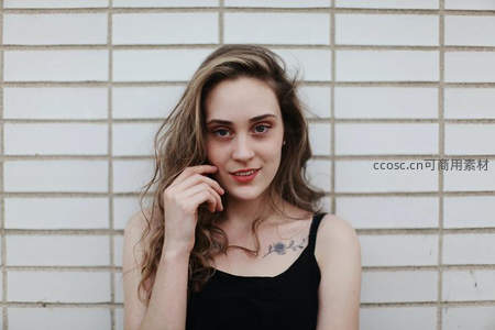 白砖墙前微笑卷发女子