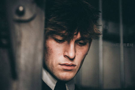 男子透过金属缝隙低眉沉思，氛围压抑神秘