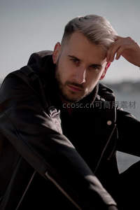 银发男子穿皮衣海边沉思望向远方
