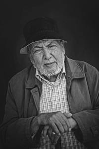 戴帽老者双手交叠，神情庄重而慈祥