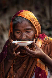 老妇双手捧碗细品热饮神情专注