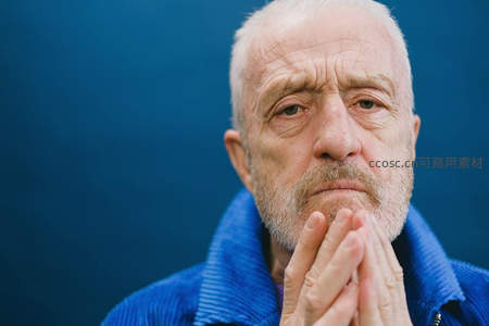 白发老者双手合十，蓝色衣领衬托沉思神情