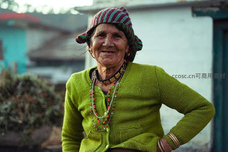 微笑的老妇人戴着彩色条纹帽，身穿绿色毛衣