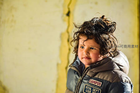 卷发孩童凝视镜头，背景斑驳墙皮