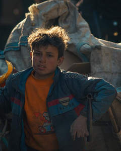 街头少年眼神坚毅，背景堆满杂物