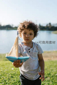 卷发男孩湖边手持玩具帆船
