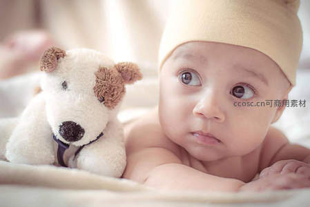 戴米色帽子与泰迪熊相伴的婴儿