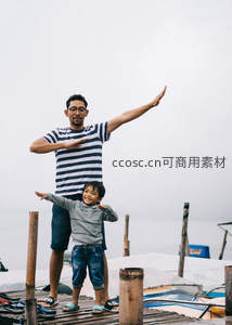 父子在码头上开心地伸展双臂，享受海边时光