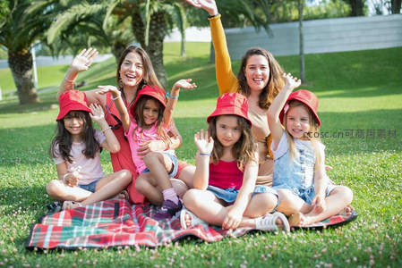 绿茵草坪上，母女们戴着红帽开心挥手合影