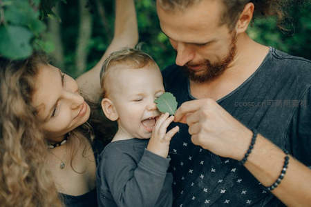 父母逗弄婴儿玩叶，自然中享受亲子乐趣