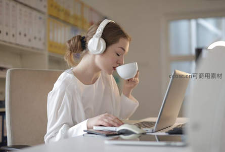 白领女性戴耳机边喝咖啡边工作