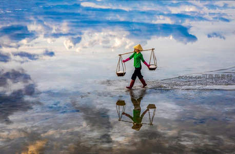 水田倒影中挑担的越南农妇