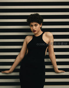 黑裙卷发女郎倚靠条纹墙